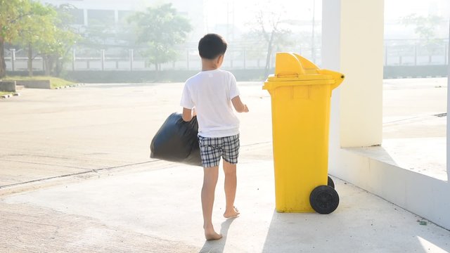 Young Asian boy carry garbage in plastic bag for eliminate in the yellow bin under the sunligh