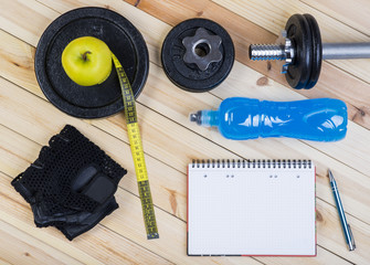 Sport Equipment. Dumbbell,  Barbell, Gloves,  Apple, Tape Measure, Isotonic Drink And Notebook To Workout Plan On Wooden Table. Sport Fitness Background