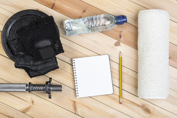 Sport Equipment. Barbell, Weight, Gloves, Towel, Bottle Of Water And Notebook To Workout Plan On Wooden Table. Sport Fitness Background