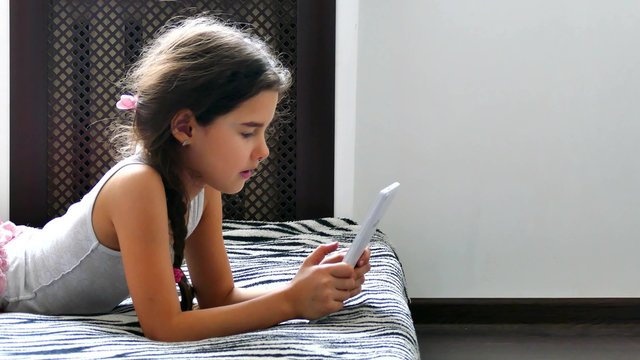 girl teen  playing tablet internet game sitting on bed 