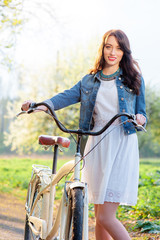 Fototapeta na wymiar Week end in park. Attractive young brunette woman walking with a bicycle against nature background.