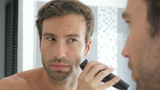 Handsome man in bathroom shaving with electric razor
