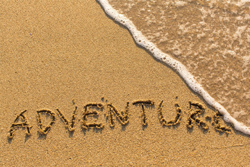 Adventure - word drawn on the sand beach with the soft wave.