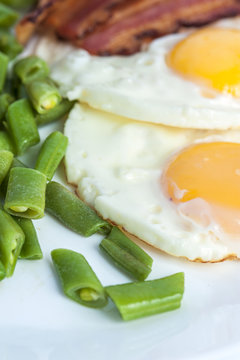 Fried eggs, bacon, green beans on light background. English breakfast. Vertical view. Focus on beans.