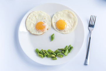 Two fried eggs with green beans on white plate, fork on light background. English breakfast. Horizontal view.