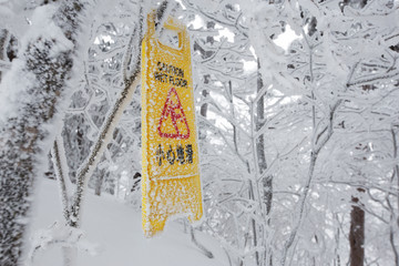 warning caution sign board on snowy trees on hill