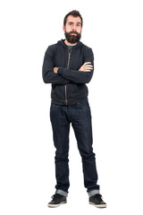 Skeptical hipster in black hooded sweatshirt with crossed arms looking at camera. Full body length portrait isolated over white studio background.