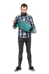 Young hipster in tartan shirt holding skateboard looking down. Full body length portrait isolated...