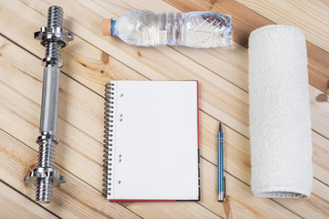 Sport Equipment. Barbell, Bottle Of Water, Towel And Notebook To Workout Plan On Wooden Table. Sport Fitness Background