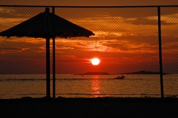 Sonnenuntergang vor einem Zaun und Sonnenschirm