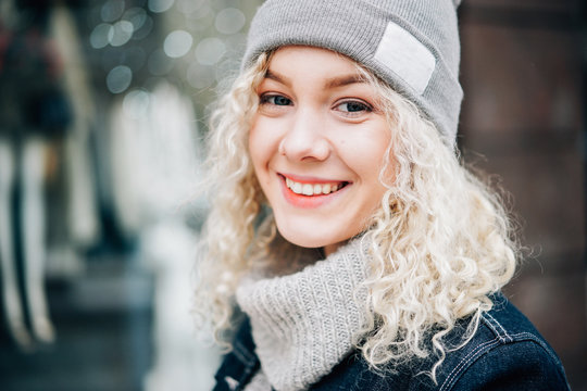 Portrait of young beautiful blond curly smiling girl in warm clothes in the street