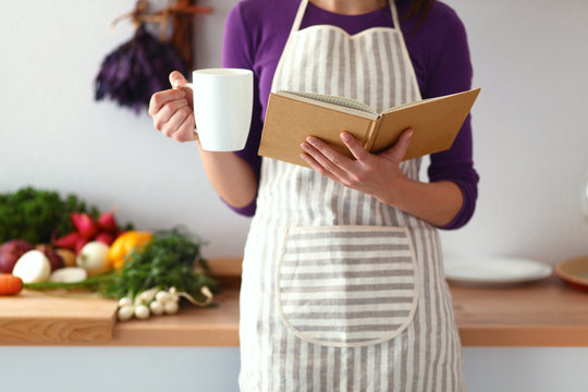 Young woman reading cookbook in the kitchen, looking for recipe
