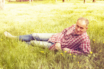 Naklejka na ściany i meble A man in a plaid shirt is resting lying on green grass.