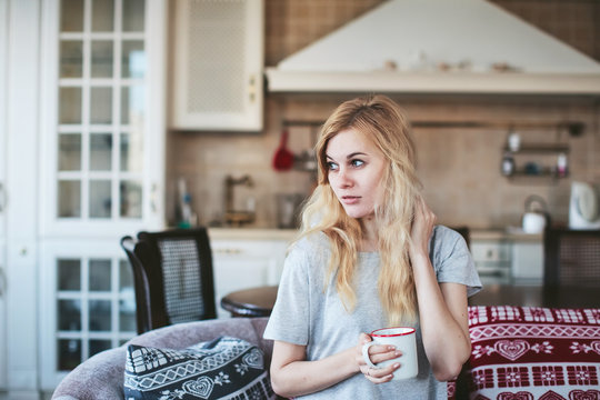 girl with a mug of tea, coffee sitting on a sofa with pillows in the kitchen
