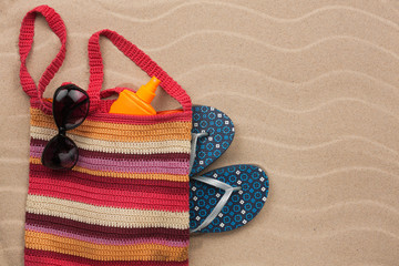 Beach bag with sunscreen, flip flops, sunglasses.