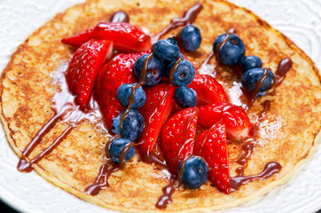 Stack of golden pancakes with strawberries, blueberries and chocolate.