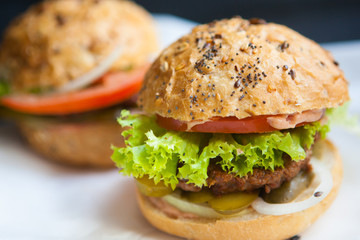 Fresh homemade burgers on wooden cutting board over dark background
