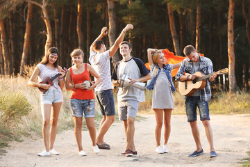 Obraz premium Happy smiling friends playing musical instruments in the forest outdoors