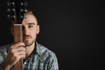 Young man with guitar on dark background