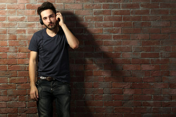 Young handsome man listening music with headphones on brick wall background