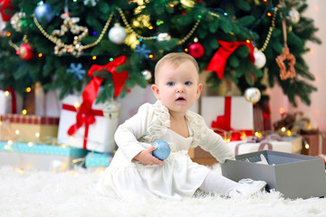 Funny baby girl with gift boxes and Christmas tree on background