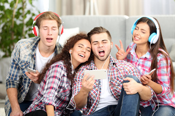 Two teenager couples listening to music and taking photo with mobile phone in living room
