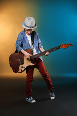 Obraz premium Little boy playing guitar on a dark lighted background