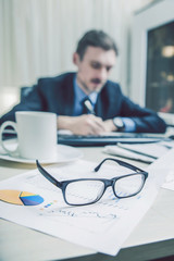 financial chart near dollars seen by unfocused glasses (only blurred out of focus silhouette of a businessman working at the Desk in the office visible viewed ) in blue color instagram