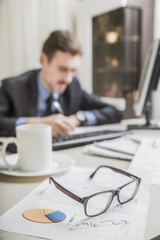 financial chart near dollars seen by unfocused glasses (only blurred out of focus silhouette of a businessman working at the Desk in the office visible viewed )