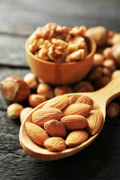 A wooden spoon, a bowl, hazelnuts, walnuts, almonds and acorns on the wooden table, close-up