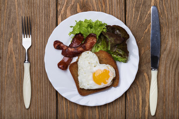 Scrambled eggs with heart shaped sausage, top view