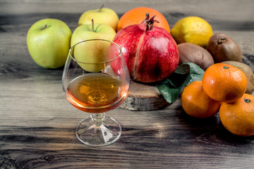 a glass of brandy with assorted tangerine kiwi apple lemon and pomegranate on Rustic Wooden Table
