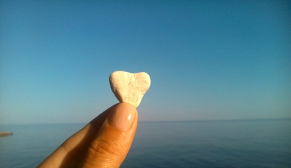 Камень в форме сердца в руке на фоне моря и синего неба