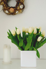 Easter arrangement with a natural egg wreath and white tulips in a vase on white background closeup