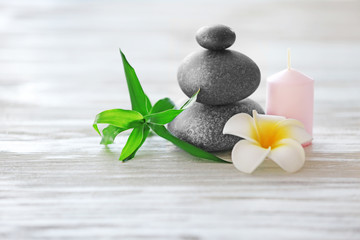 Spa stones with candle, bamboo and tropical flower on light wooden background