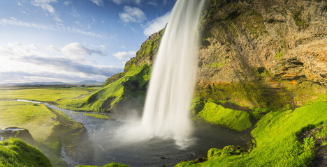 lumières chaudes du soleil et cascade avec canyon vert et ciel bleu en Islande