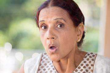 Closeup portrait, elderly woman in white dress taken aback, blown away, by what she sees or hears, isolated outdoors outside background with green trees