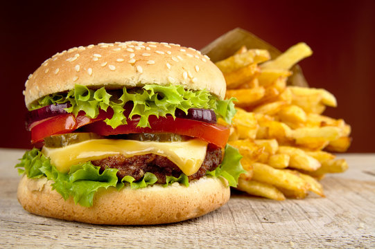 Cheeseburger and french fries on red spotlight on wooden table
