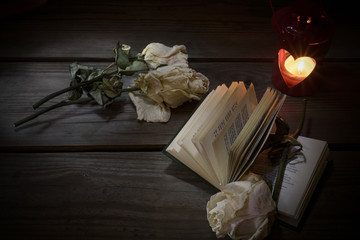Open book, dry rose and candle on an old wooden table