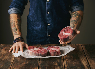 butcher with tattooed hands offers raw meat steak