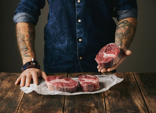 Butcher With Tattooed Hands Offers Raw Meat Steak