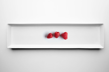 Three raspberries isolated on white ceramic plate