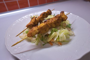 Chicken curry skewer served on the top of vegetable salad made from lettuce and other leaves served on the simple rustic white plate. Fresh and health dish with balanced nutritions for reduction diet.