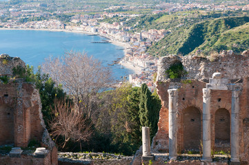 View of some columns in the scene of the greek theater in Taormina and a perspective of Giardini Naxos in the background