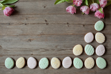  Easter cookies in the shape of an egg painted with sugar icing on a wooden table, tulips and space for text