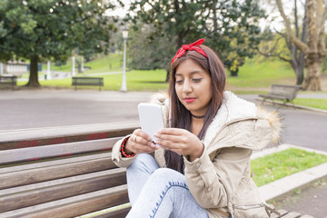 Woman sitting on bench and looking messahe her smartphone.