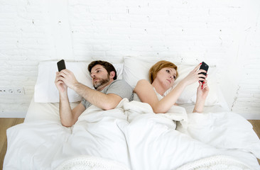 young married couple using their mobile phone in bed ignoring each other in relationship...