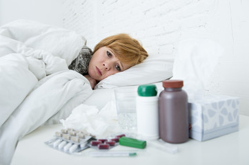 Obraz na płótnie Canvas sick woman feeling bad ill lying on bed suffering headache winter cold and flu virus having medicines