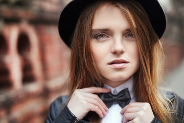 Close up street portrait of young beautiful lady holding the bow-tie and looking at camera. Girl wearing stylish black and white clothes. Female fashion. Toned