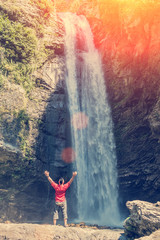 Rear view of man with hands up standing near waterfall 89503182802